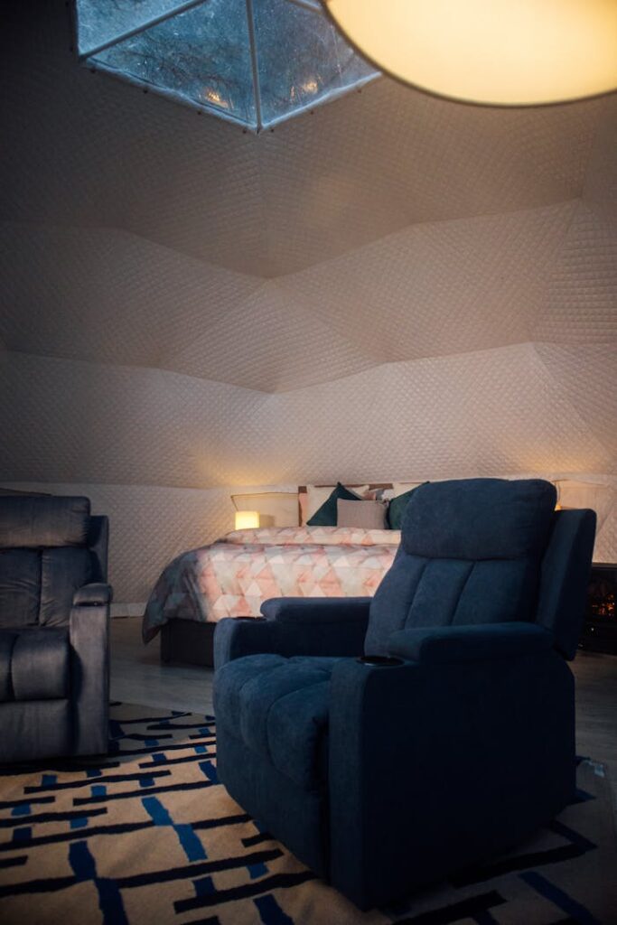 Comfortable bedroom with stylish recliner, cozy bed, and warm ambient lighting creating a relaxing atmosphere.