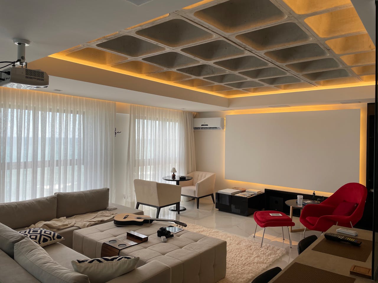 Spacious minimalist living room with natural light, featuring cozy seating and a ceiling projector.